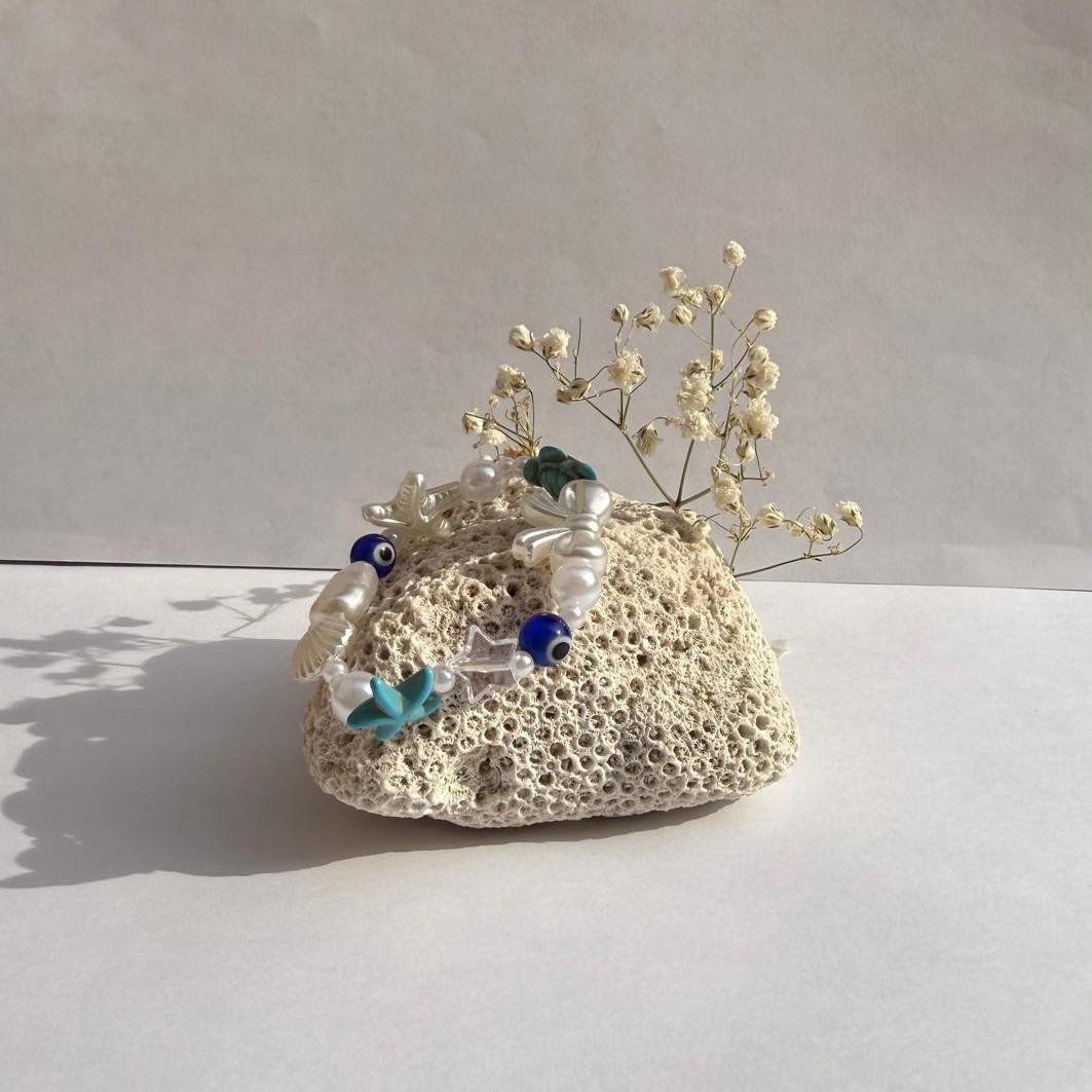 Blue Lagoon bracelet on a rock with flowers against a white wall