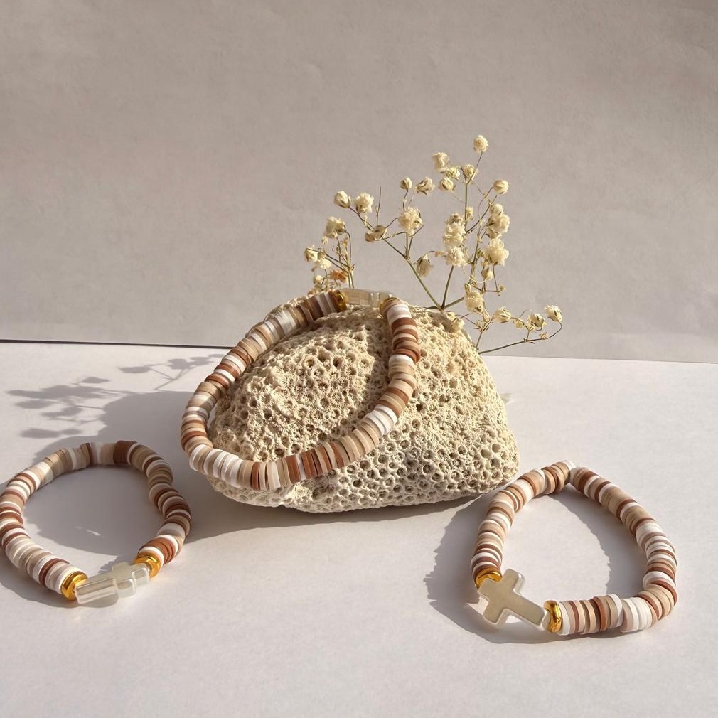Coconut Cross bracelets on both sides of a rock with flowers against a white wall