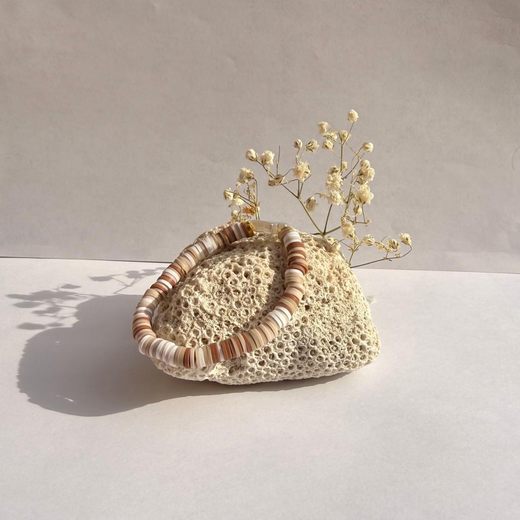 Coconut Cross bracelet on a rock with flowers against a white wall