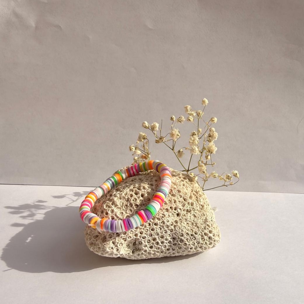 Confetti Pop rainbow bracelet on a rock with flowers against a white background