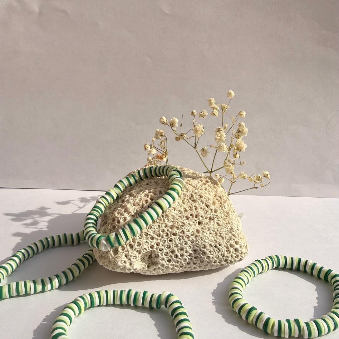 Jade Stripe bracelets around a rock with flowers against a white background