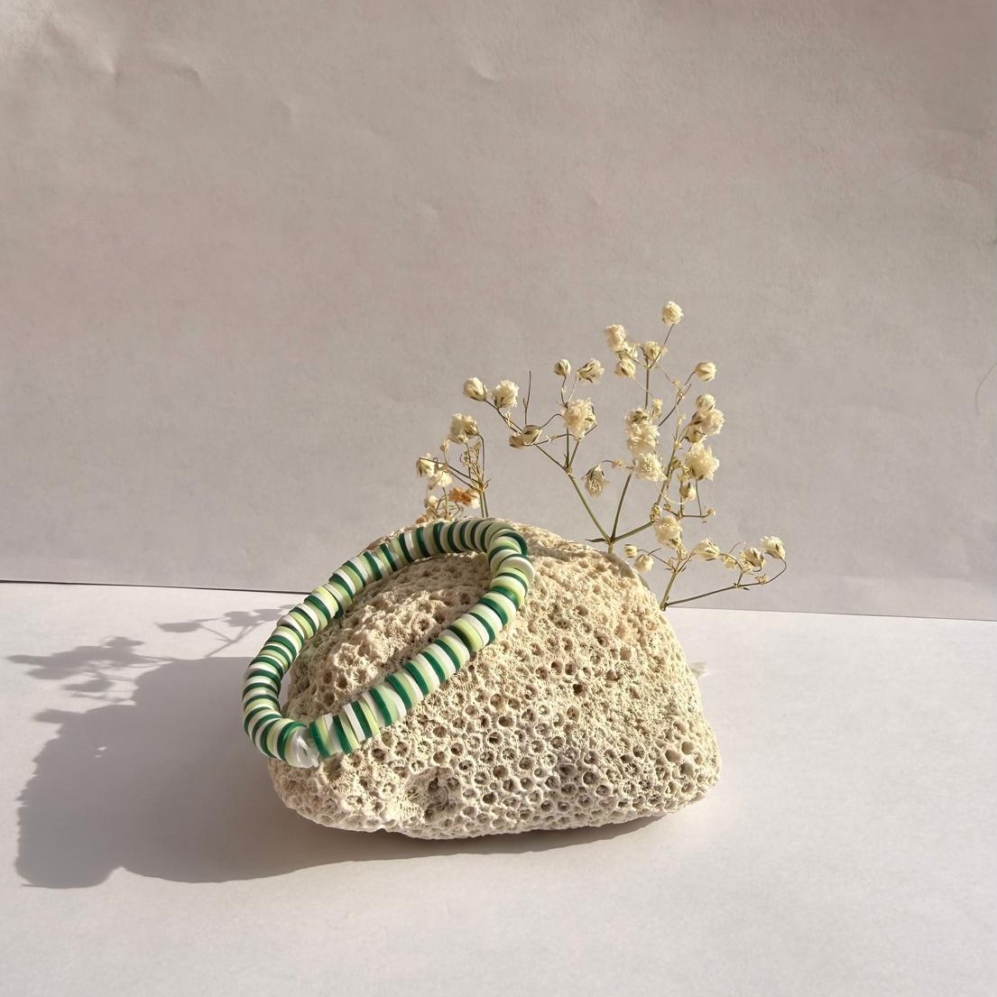 Jade Stripe bracelet with forest green, mint, and creamy white striped beads on a rock with flowers
