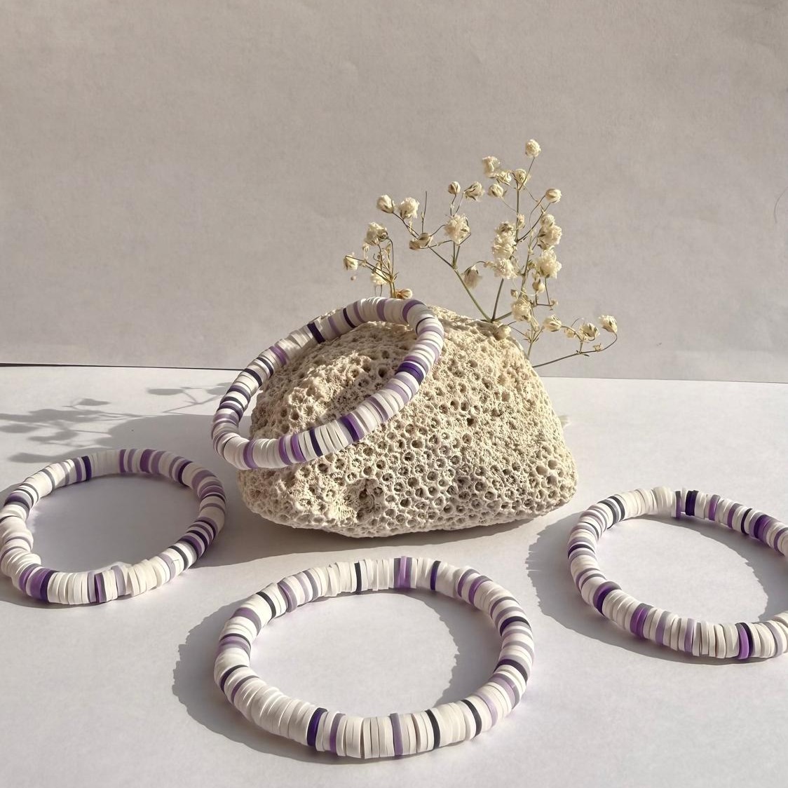 Lavender Cloud bracelets arranged around a rock with white flowers