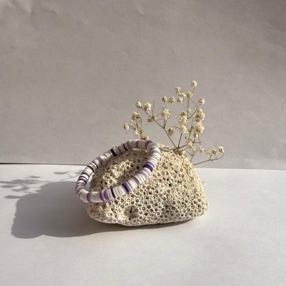 Lavender Cloud bracelet on a rock with flowers against a white wall