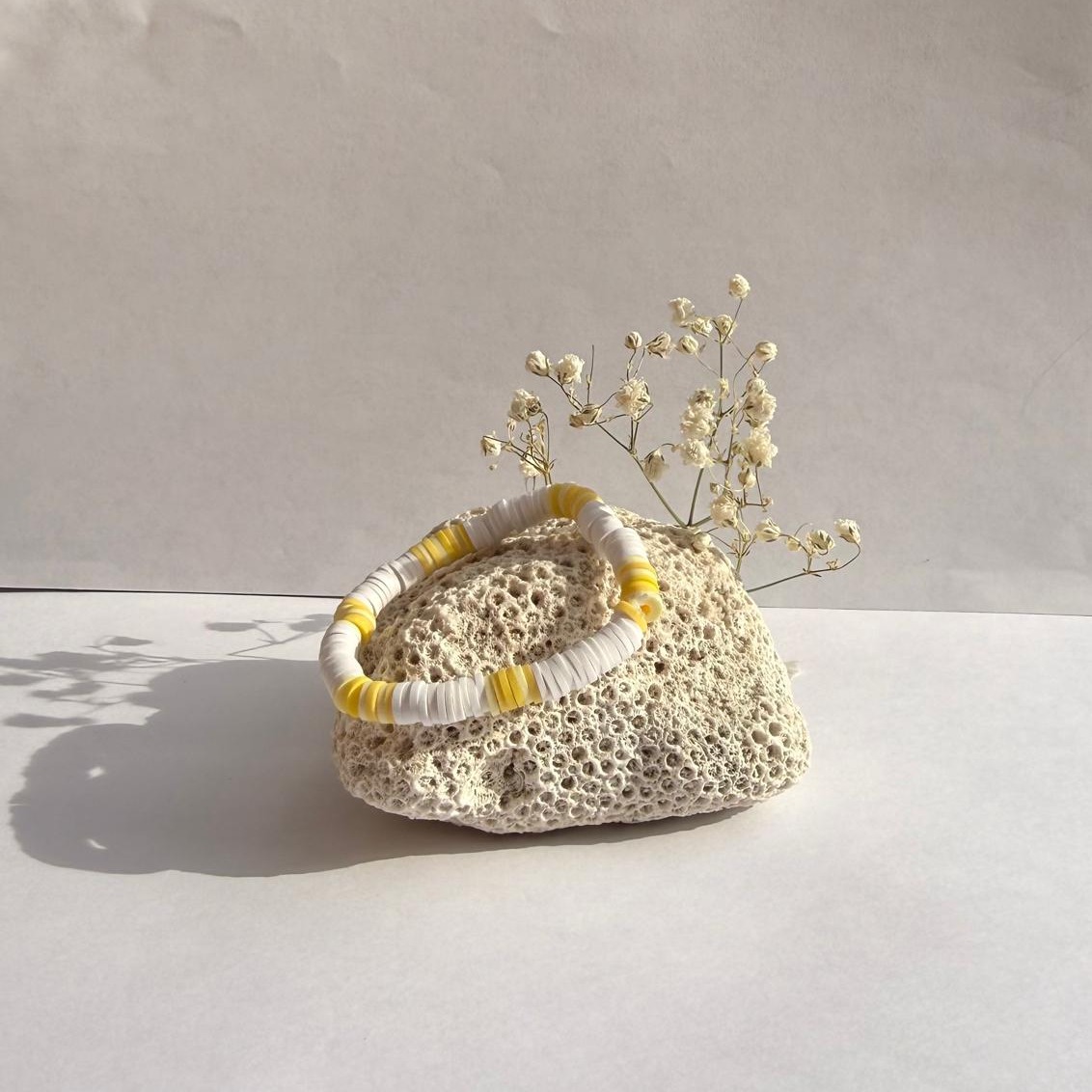 Lemon Drop bracelet on a rock with flowers against a white wall