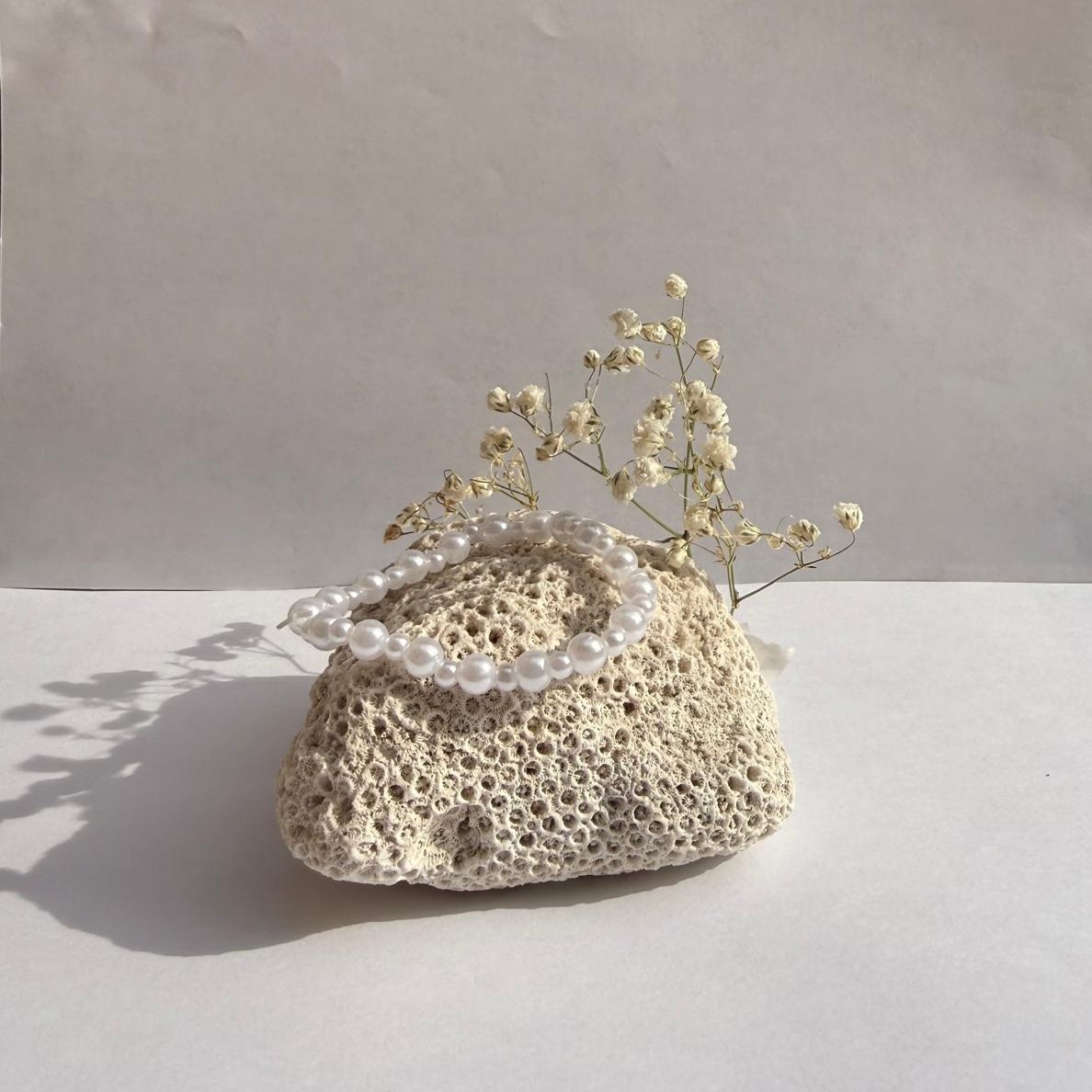 Pearl Pop bracelet on a rock with flowers against a white wall