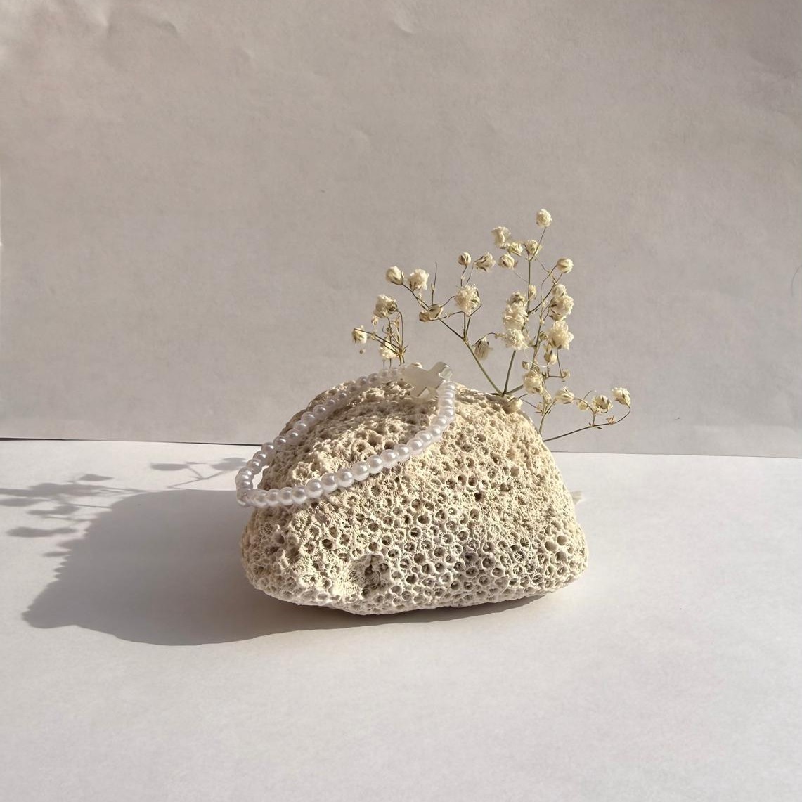 Pearl Prayer bracelet on a rock with flowers against a white wall