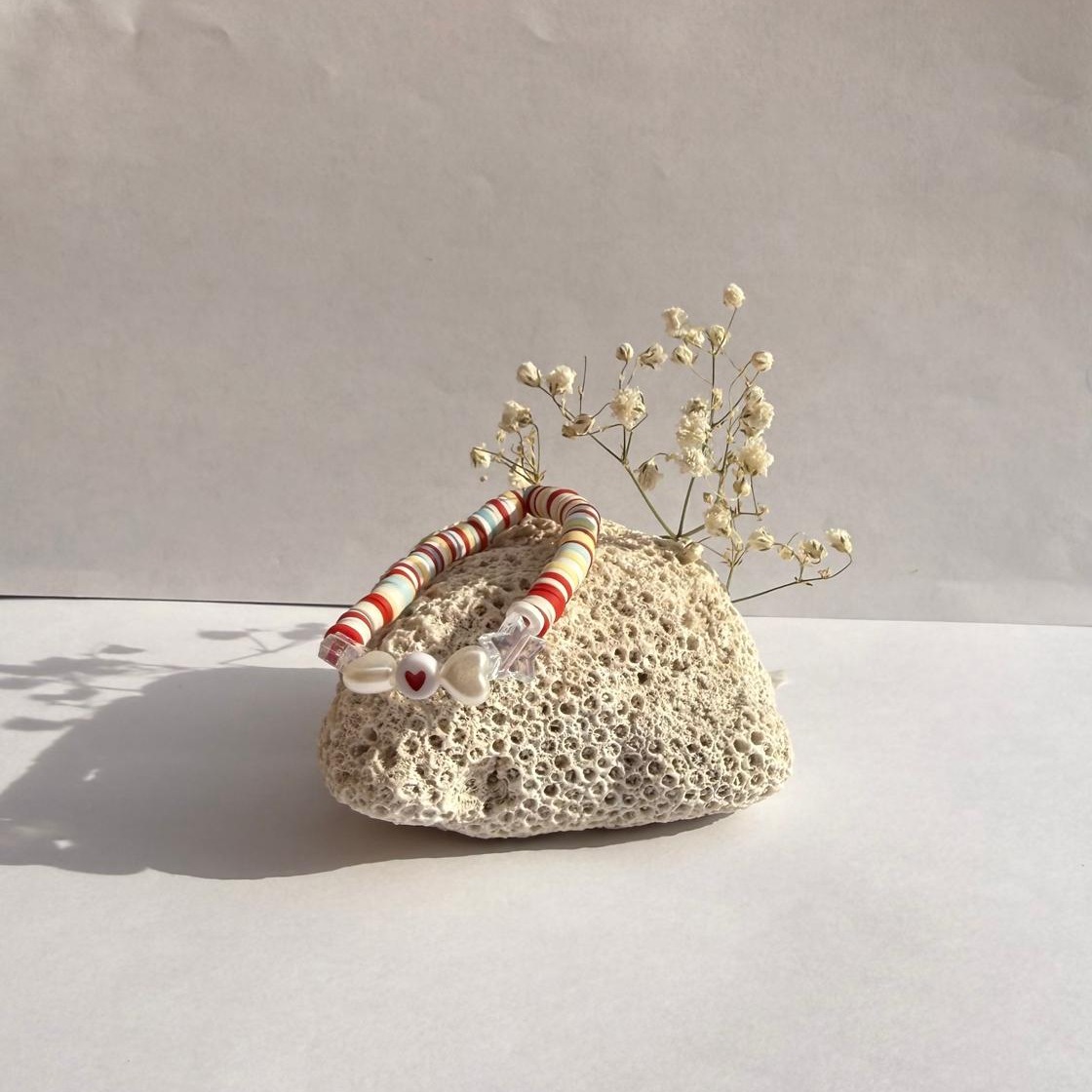 Red Ribbon bracelet on a rock with flowers against a white wall