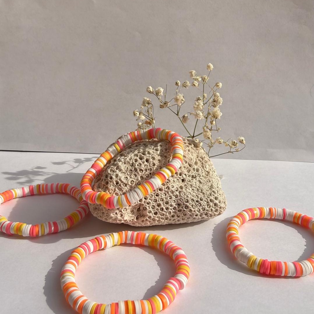 Sherbet Sunset bracelets around a rock with flowers against a white wall