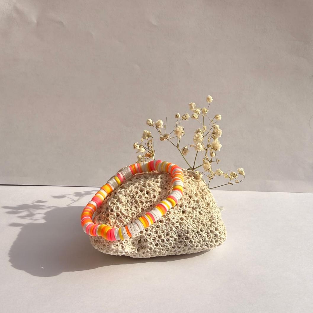 Sherbet Sunset bracelet on a rock with flowers against a white wall