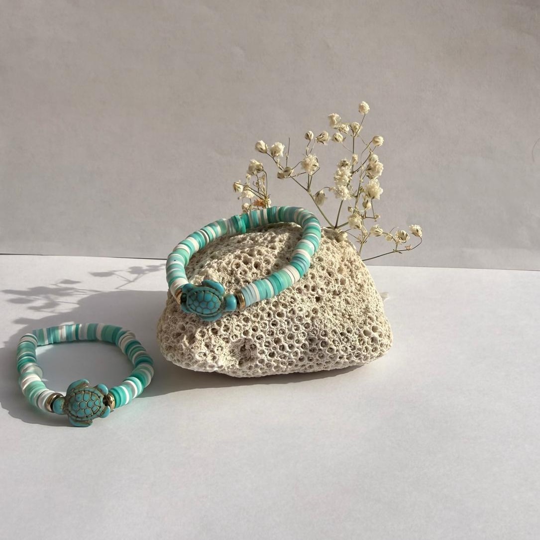 Teal Pop bracelets arranged around a rock with white flowers