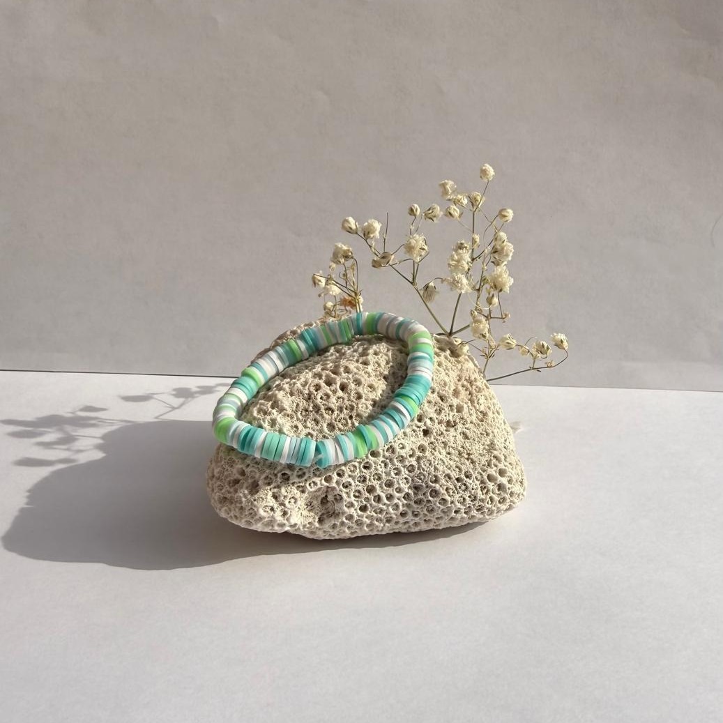 Turquoise Tide bracelet on a rock with flowers against a white wall
